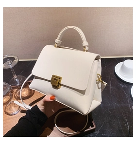 Close-up of beige leather small square bag with gold metal buckle on marble surface