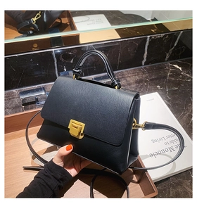 Detailed view of black litchi texture leather handbag with gold matte metal push-lock