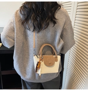 Detail of a chic two-tone crossbody bag with elegant top handle and beaded charm on model