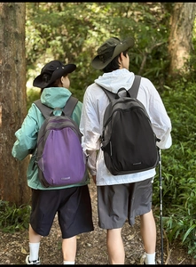 Outdoor backpacks in purple and black colors shown in a forest trail setting