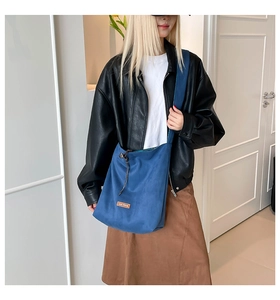 Detail of blue canvas tote bag featuring brown leather logo patch and adjustable strap