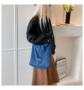 Detail of blue canvas tote bag with drawstring design and leather tag on a model