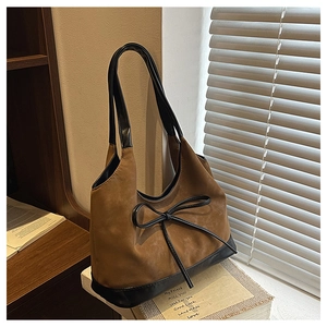 Detail of suede bucket bag with leather bow accent on a stack of vintage books