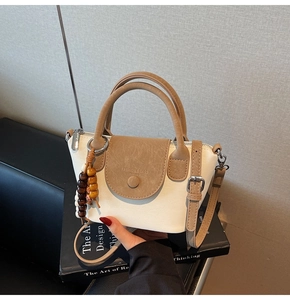 Detailed close-up of cream and beige crossbody bag with fashion stamp and wood bead charm