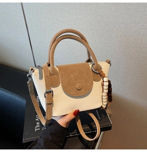 Detail of elegant two-tone shoulder bag featuring a beaded pendant and magnetic flap closure