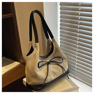 Detail of a half-moon bucket bag featuring faux suede texture and a black leather bow