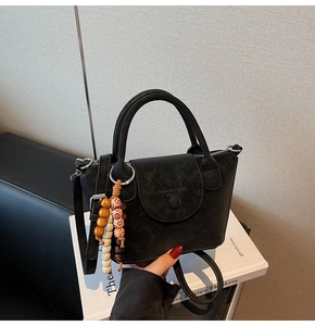 Detail of vintage black PU leather handbag featuring wooden bead charm and metal hardware
