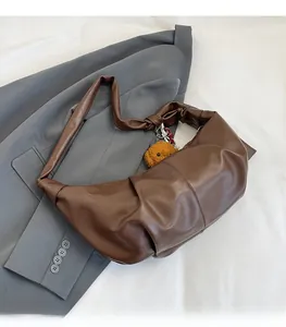 Detail of dark brown pleated tote bag with plush bear charm on grey blazer backdrop