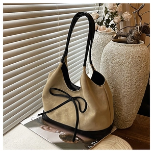 Close-up of beige suede bucket bag with black leather base and decorative bow detail