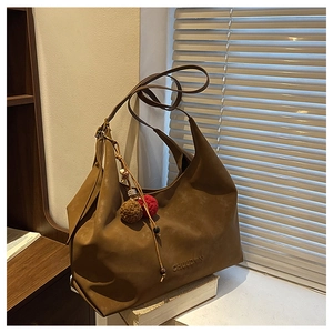 Détail d'un sac hobo en cuir marron avec des pompons bicolores et des perles décoratives