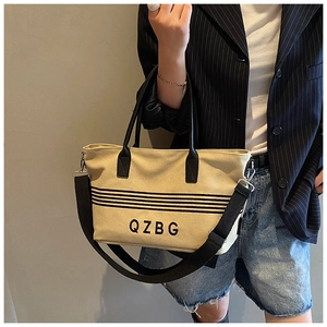 Detail view of canvas tote bag with black stripes and embroidered QZBG logo on the front