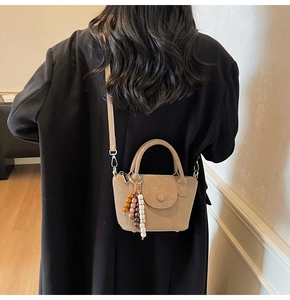 Detail of apricot matte leather handbag with decorative beaded charm and shoulder strap
