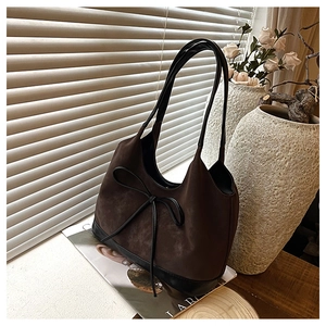 Detail of dark brown suede bucket bag with a bow accent and black leather base