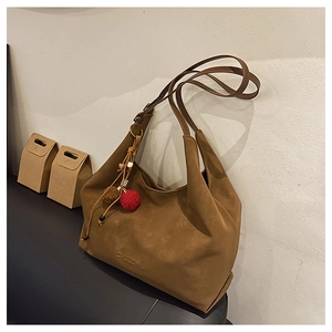 Détail du sac cabas en daim marron avec logo CHUU DON et breloque pompon rouge décoratif