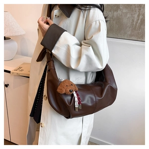 Detail of dark brown PU leather crescent bag with knot strap and teddy bear charm on model