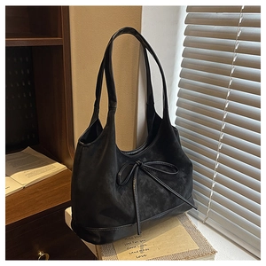 Detail of black matte suede bucket bag with decorative bow placed on books by a window