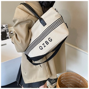 Close-up of beige striped canvas tote bag featuring black leather handles and adjustable strap