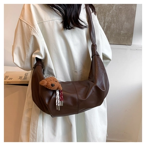 Detailed view of brown matte leather moon bag with teddy bear charm on model in trench coat