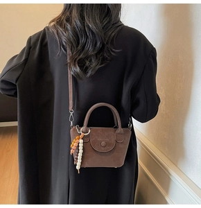 Detail of dark brown crossbody bag with colorful bead charm on a black wool coat