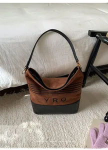 Detail of hobo bag featuring brown suede body with quilted black leather base and YRO logo