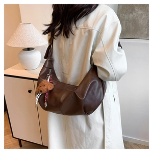 Detail of a dark brown crescent bag with a plush bear charm worn with a beige trench coat