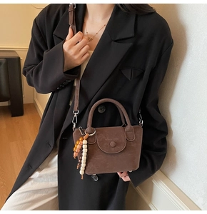 Detail view of dark brown retro shoulder bag with beaded charm and matte leather texture