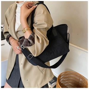 Detail of black striped canvas tote bag with QZBG embroidery worn with a trench coat