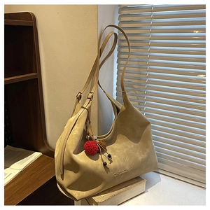 Détail du sac fourre-tout en daim kaki avec logo embossé et breloque pompon rouge et ombres