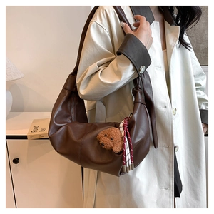 Detail of dark brown leather dumpling bag with plush bear charm and woven rope