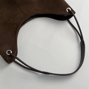 Detail of dark brown suede shoulder bag showing silver eyelet and thin leather strap