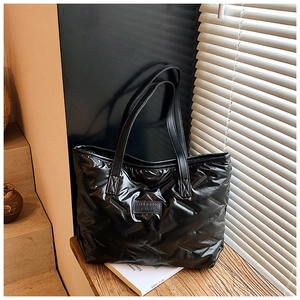 Detail view of black quilted puffer tote bag with glossy finish and brand logo