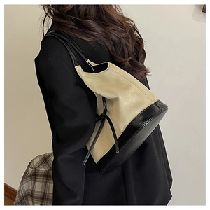 Detail view of contrast stitching and black leather strap on minimalist beige bucket bag