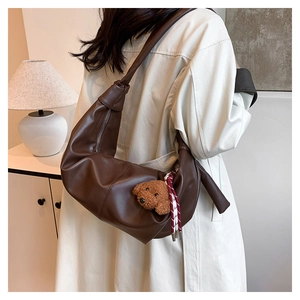Detail of dark brown leather crescent bag featuring knot strap and plush dog charm