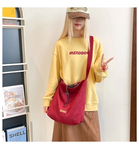 Detail of red oversized crossbody tote bag with drawstring closure and brand metal tag