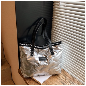 Detail showing the silver metallic quilted texture and logo patch of the tote bag