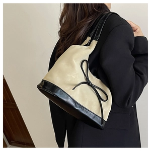 Close-up of suede shoulder bag featuring a black leather bow and stylish contrast base