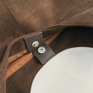 Detail of the magnetic closure on a brown suede tote bag with precision stitching
