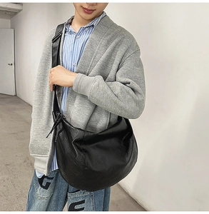 Sac bandoulière demi-lune noir minimaliste avec large sangle porté par un mannequin