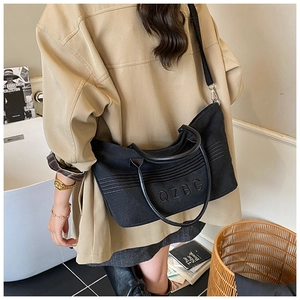 Detail of a large black canvas tote bag with QZBG embroidery worn as a crossbody bag