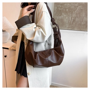 Close-up of dark brown leather shoulder bag featuring unique knotted strap and metal ring detail