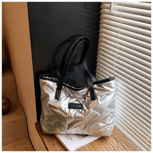 Detailed view of silver quilted tote bag with black leather straps on a wooden windowsill