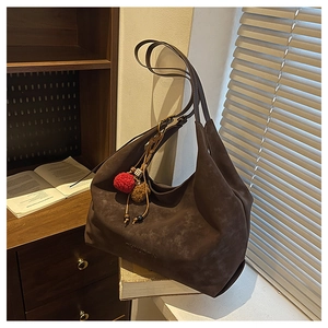 Détail d'un grand sac hobo marron foncé avec pompon coloré et logo embossé en daim