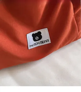 Macro detail of Myron Bear black bear logo and brand tag on orange canvas bag fabric