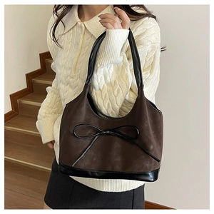 Detail of dark brown suede bucket bag with black leather bow and textured finish