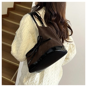 Detail of brown suede bucket bag with black bow and patent leather base on shoulder