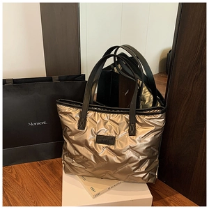 Detail of metallic gold quilted tote bag with black leather handles and rubber logo patch