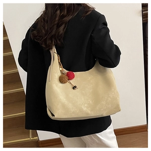 Détail d'un sac cabas en cuir beige avec pompons en peluche et logo de marque