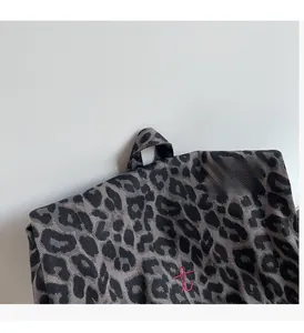 Detailed close-up of leopard print canvas backpack with reinforced top handle and red embroidery