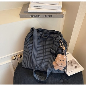 Close-up of a blue checkered bucket bag with a cute brown bear charm on soft padding