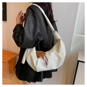 Detail of off-white faux leather half-moon bag featuring pleated texture and bear charm
